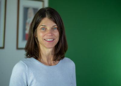 Middle-aged woman with shoulder-length dark brown hair, standing in front of a dark green wall